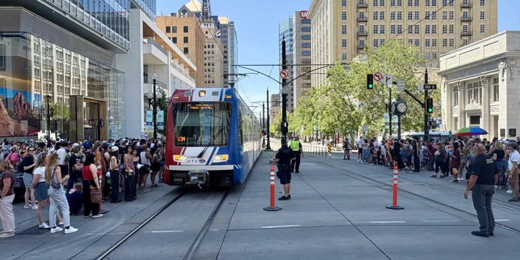 A UTA Trax train is guided through the Pride parade crowds at City Center Station.